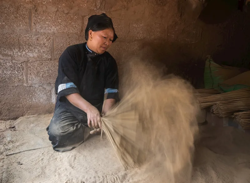Một phụ nữ mặc áo đen truyền thống đang phủ bột mùn cưa lên tăm hương trong xưởng gần Cao Bằng.