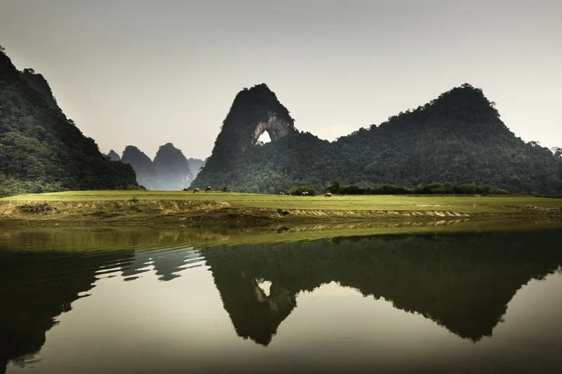 Ngọn núi đá vôi hình con mắt soi bóng xuống mặt hồ tĩnh lặng bên đồng cỏ xanh ở Cao Bằng.
